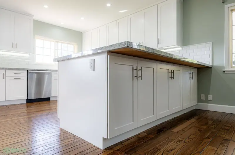 A modern kitchen remodel featuring white shaker-style cabinets, a granite-topped kitchen island with silver hardware, and dark hardwood flooring.