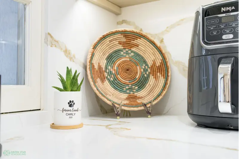 Modern kitchen countertop with a white marble backsplash, featuring a small potted succulent dedicated to "Carly 2021," a decorative woven basket, and a Ninja Max air fryer.