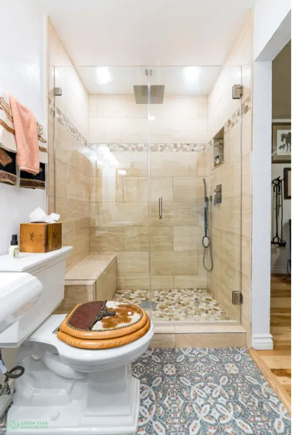 A bathroom remodel by Green Star Remodeling featuring a walk-in glass shower with tan wall tiles, a built-in bench, pebble floor, a handheld showerhead, and patterned floor tile.