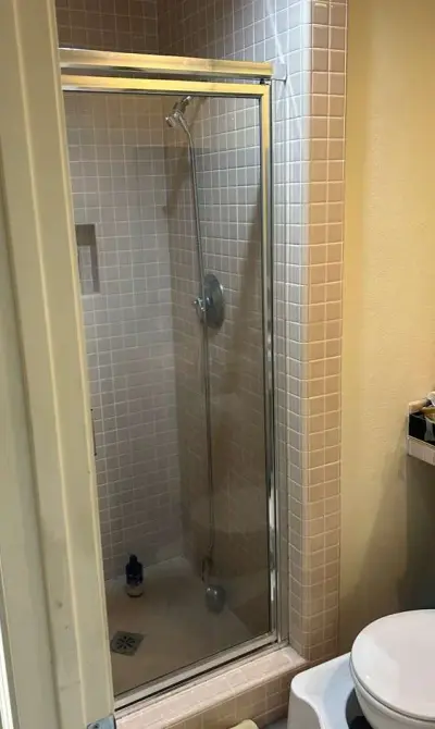 A modern small bathroom featuring a walk-in shower with a glass door and light pink square mosaic tiles on the walls.
