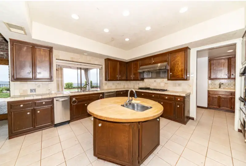 A spacious kitchen featuring dark wood cabinetry, a tiled backsplash, and a unique round butcher block kitchen island with a built-in stainless steel sink.