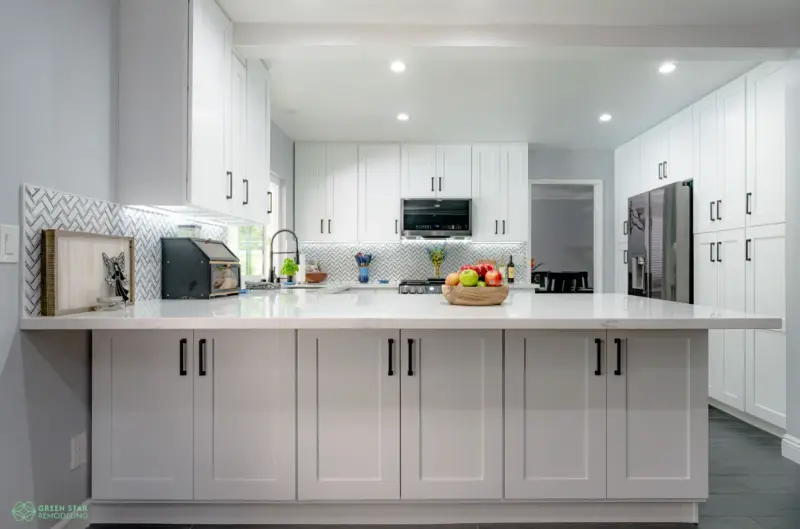 A modern kitchen remodel by Green Star Remodeling in Santa Clarita featuring white shaker-style cabinets, a large white quartz island, and a herringbone pattern tile backsplash.
