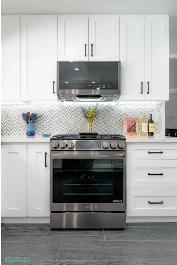 A modern kitchen remodel by Green Star Remodeling featuring white shaker cabinets, a stainless steel LG stove and over-the-range microwave, a white herringbone tile backsplash, and dark grey wood-look flooring.