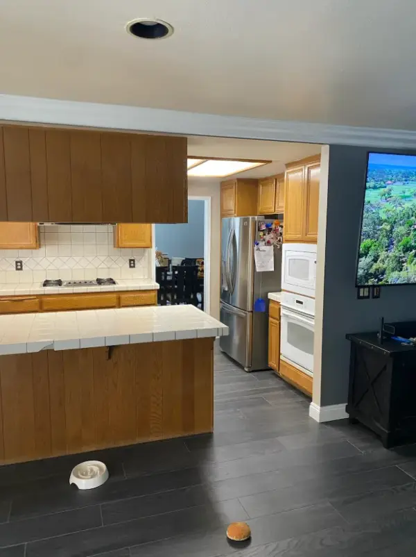 A kitchen featuring dark wood-look tile flooring, light oak cabinetry, white tiled countertops, and stainless steel appliances, including a French door refrigerator and built-in white double oven.