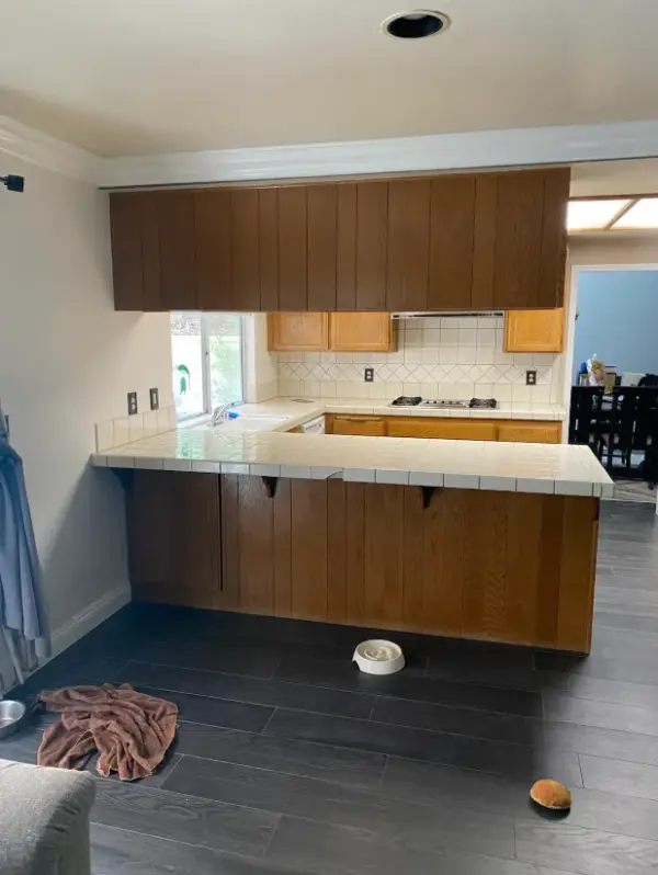 A kitchen featuring dark gray wood plank flooring, light oak cabinetry, and a large peninsula with white tile countertops, stainless steel appliances, and a white built-in wall oven and microwave.