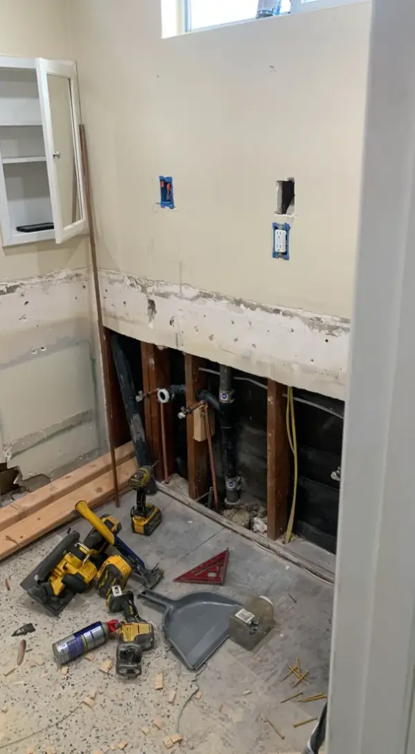 A bathroom undergoing professional remodeling, showing exposed wall studs with new copper plumbing lines, black drain pipes, and rough-in electrical outlet boxes installed.