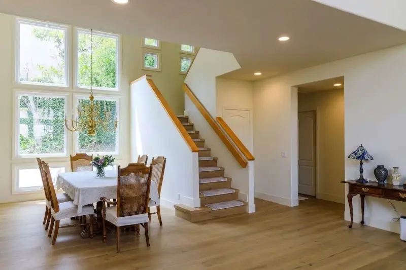 Dining area adjacent to the staircase, featuring a large dining table with high-backed chairs, a chandelier, and wood flooring.