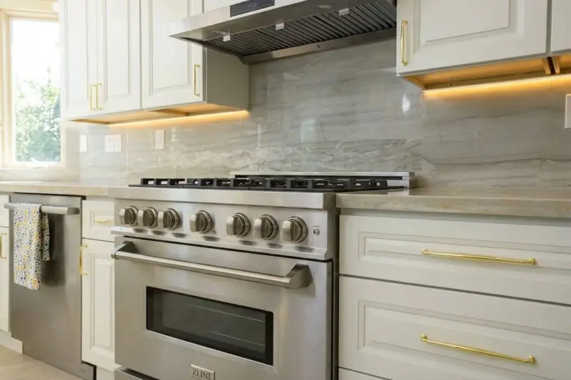 Perspective view of the stainless steel professional gas range, gold drawer pulls, and white cabinetry.