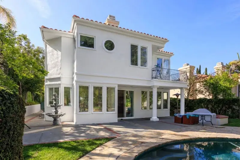 Rear exterior view of the white home showcasing the backyard patio, swimming pool, fountain, and second-story balcony.