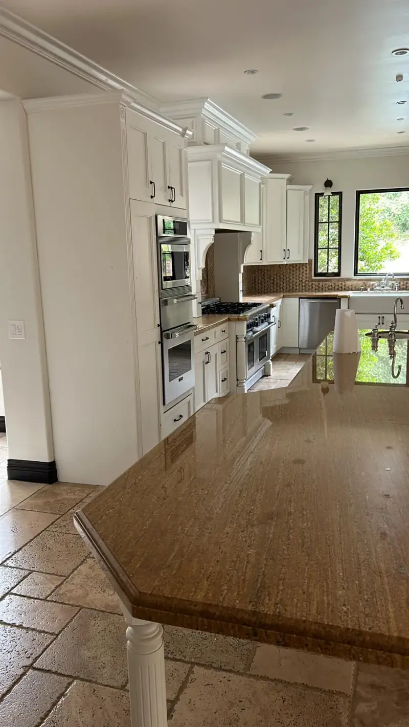 Luxury white kitchen with a brown granite island and travertine floors in Calabasas.