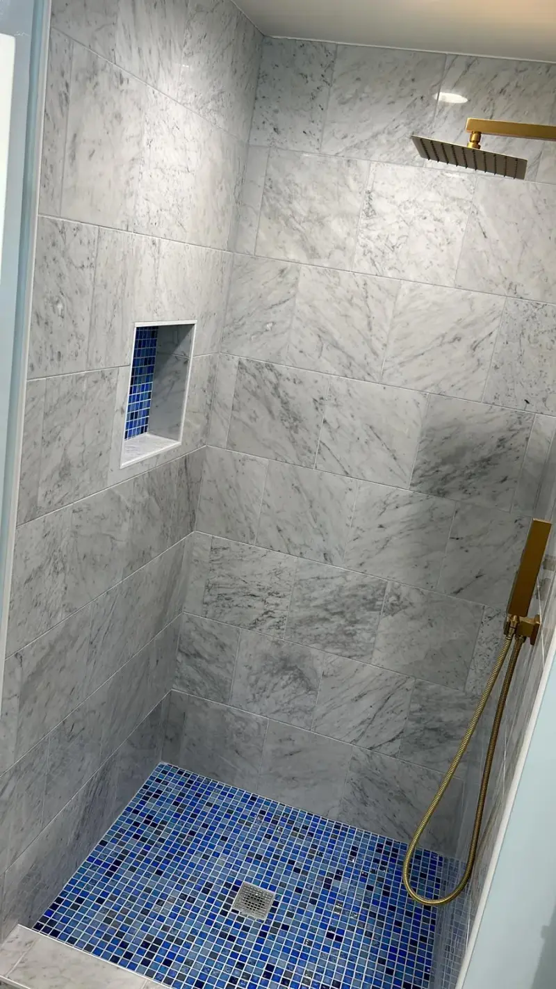 Marble-tiled walk-in shower with a blue mosaic floor in a Woodland Hills bathroom remodel.