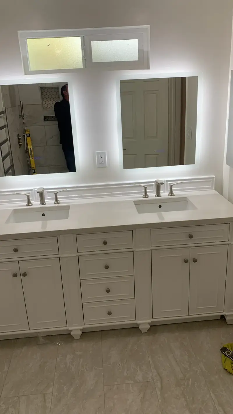 A contemporary white double bathroom vanity featuring two rectangular sinks, silver faucets, and two square mirrors with integrated LED backlighting.